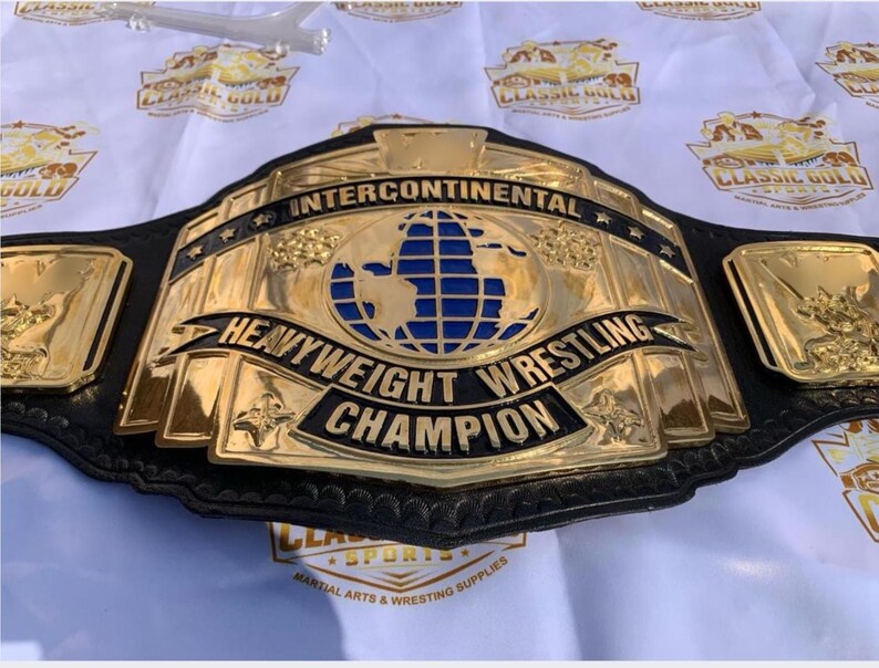May include: A gold and black Intercontinental Heavyweight Wrestling Champion belt. The belt features a large central plate with a blue and gold globe design, and the words "Intercontinental Heavyweight Wrestling Champion".