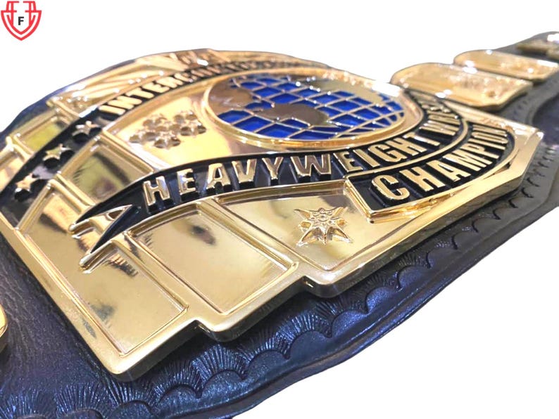 May include: Close-up of a gold and black heavyweight championship belt. The belt features the words "International Heavyweight Champion" and a blue globe design. The belt is made of gold-colored metal and black leather.