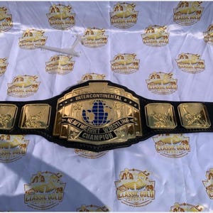 May include: A gold and black Intercontinental Heavyweight Wrestling Champion belt. The belt has a large gold center plate with a blue globe design and the words "Intercontinental Heavyweight Wrestling Champion". The belt also has several smaller gold plates with wrestling figures.