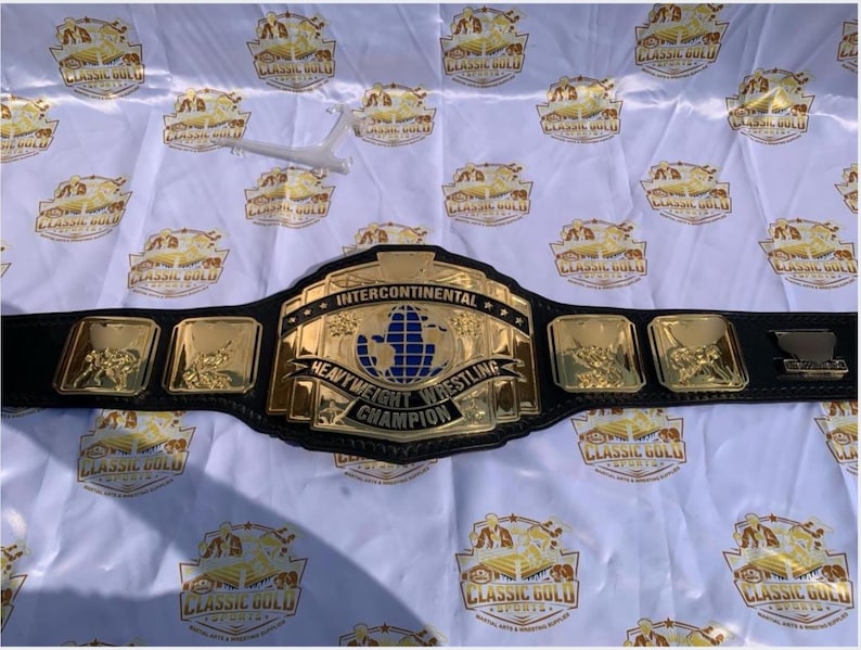 May include: A gold and black Intercontinental Heavyweight Wrestling Champion belt. The belt has a large gold center plate with a blue globe design and the words "Intercontinental Heavyweight Wrestling Champion". The belt also has several smaller gold plates with wrestling figures.
