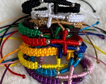 May include: A stack of colorful knotted bracelets with silver beads and a cross charm. The bracelets are in the colors black, white, brown, green, red, yellow, blue, purple, and pink.