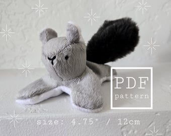 Könnte beinhalten: Ein graues Plüsch-Eichhörnchen-Spielzeug mit einem schwarzen, flauschigen Schwanz und weißen Akzenten. Das Spielzeug ist etwa 12 cm lang. Das Bild enthält den Text "PDF pattern".