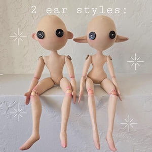 May include: Two handmade cloth dolls with button eyes and articulated limbs. The dolls are nude with two different ear styles, one with round ears and the other with pointed ears. The text "2 ear styles:" is above the dolls.