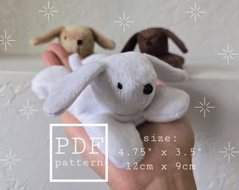 Könnte beinhalten: Drei Plüsch-Hasenspielzeuge in Weiß, Beige und Braun werden in einer Hand gehalten. Der weiße Hase ist im Vordergrund. Das Bild enthält den Text "PDF pattern" und Größenangaben von 12cm x 9cm.