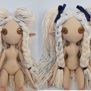 May include: Two handmade cloth dolls with button eyes and yarn hair. One doll has its hair styled in two buns, while the other has long braids tied with blue ribbons. Both dolls have pointed ears and are made of beige fabric.
