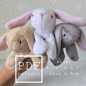 May include: Three plush bunny toys in beige, white, and gray, each with long ears and embroidered facial details. The size is 4.75" x 3.5". The image includes the text "PDF pattern".