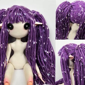 May include: A handmade doll with a fabric body and long, purple yarn hair. The doll has large black button eyes, small pointed ears, and a neutral skin tone. The hair is styled in two long pigtails with white and blue flecks.