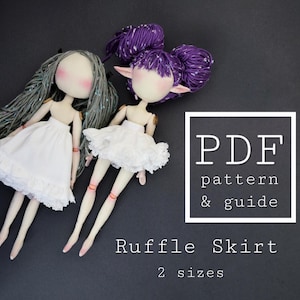May include: Two handmade dolls with light skin, one with long gray yarn hair and one with purple yarn hair styled in two buns. Both dolls wear white ruffled skirts. Text on the image reads: PDF pattern & guide, Ruffle Skirt, 2 sizes.