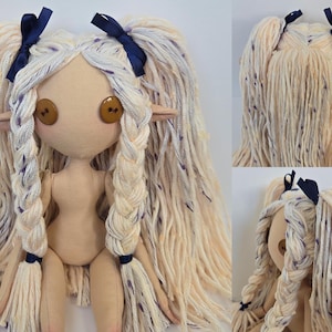 May include: A handmade cloth doll with long, cream-colored yarn hair, styled in braids and pigtails, accented with navy blue ribbons. The doll has button eyes and pointed ears, with a neutral skin tone.