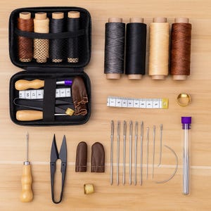 May include: A black sewing kit with spools of brown, beige, and black thread. The kit contains a measuring tape, needles, scissors, thimble, and other sewing tools. The items are arranged on a light wood surface.