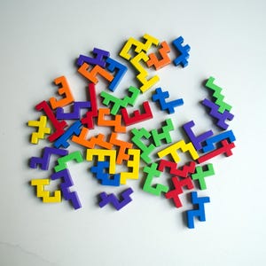 May include: A collection of colorful, geometric puzzle pieces in various shapes and sizes. The pieces are in shades of red, blue, yellow, green, orange, and purple. The puzzle pieces are scattered on a white surface.