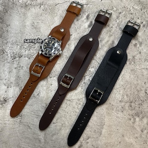 Könnte beinhalten: Drei Leder-Armbänder in Braun-, Dunkelbraun- und Schwarztönen. Eines der Bänder hält eine silberne Uhr mit schwarzem Zifferblatt. Jedes Armband hat eine Schnalle und ist für das Handgelenk konzipiert. Das Wort "sample" ist sichtbar.