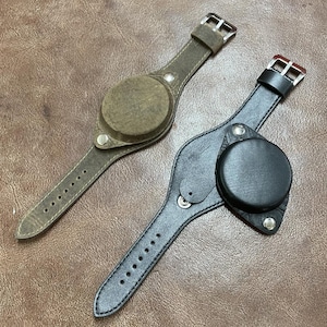 May include: Two leather watch straps with a round watch face cover. One strap is brown with a light brown cover and the other is black with a black cover.