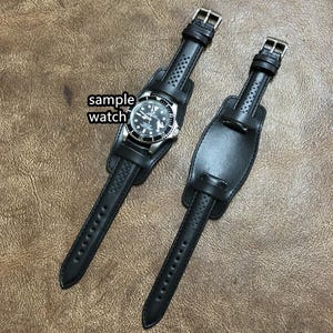 May include: Two black leather watch straps with a silver watch face. The strap on the left has a buckle closure and the strap on the right has a velcro closure.