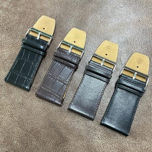 Puede incluir: Cuatro correas de reloj en tonos marrones y negros. Dos correas tienen una textura similar a la piel de cocodrilo, mientras que las otras son lisas. Cada correa tiene una hebilla plateada y un respaldo de cuero color canela. Para un reloj de 40 mm.