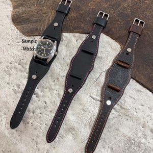 Op de afbeelding: Drie leren horlogebandjes in zwart en bruin, met zilveren gespen en klinknagels. Eén bandje houdt een horloge met een zwarte wijzerplaat vast. De zwarte bandjes hebben roze stiksels. Het bruine bandje heeft bruine stiksels en houten accenten. De tekst "Sample Watch" is zichtbaar.