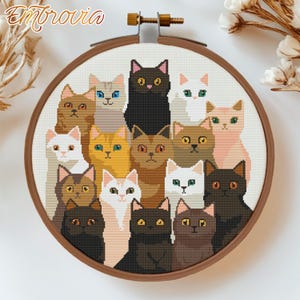 Peut inclure: Un cercle de broderie rond avec un fond blanc et un motif de 16 chats de différentes couleurs et motifs. Les chats sont disposés en cercle autour du cercle, la tête face au spectateur.