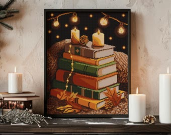 May include: A framed cross-stitch artwork depicts a stack of books with autumn leaves, lit candles, and string lights against a dark background. The artwork has a cozy, warm aesthetic, with a black frame and the word "Embrovia" at the bottom.