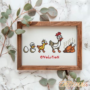 May include: Cross-stitch artwork in a wooden frame depicts the evolution of a chicken, from egg to roasted fowl. The design features pixelated images of a hatching chick, a duckling, a hen, and a cooked chicken. The word "OVeLutioN" is stitched below the images.
