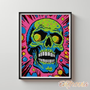 May include: A framed cross-stitch art piece featuring a colorful skull design. The skull is rendered in shades of blue, green, and black, with yellow eyes and a white toothy grin. The background is a vibrant pink with bursts of color.