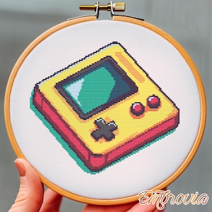 May include: A cross-stitch pattern of a yellow and red handheld video game console with a green screen. The console has a red button on the top right and a black button on the bottom.