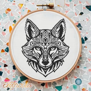 May include: A black and white cross-stitch fox design in a wooden embroidery hoop. The fox has intricate patterns and details. The word "Embrovia" is written in a cursive font at the bottom of the hoop.