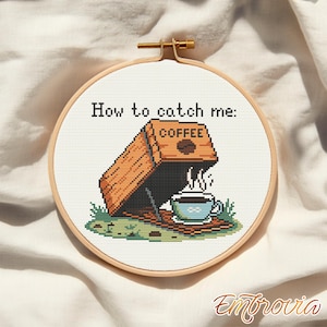 May include: A cross-stitch embroidery hoop with the text "How to catch me:" above a coffee-themed design. The design features a coffee maker, a steaming coffee cup, and the word "COFFEE". The hoop is set against a neutral fabric background.