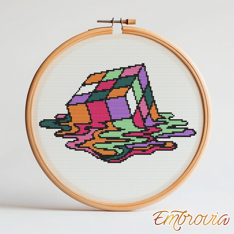 May include: A colorful cross-stitch design of a melting geometric shape, framed in a wooden embroidery hoop. The artwork features a vibrant palette of pink, orange, green, and purple. The word "Embrovia" is written in cursive at the bottom.