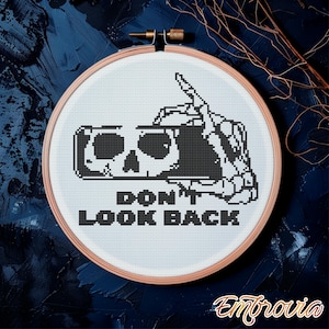 May include: A cross-stitch embroidery hoop featuring a black and white skull design with a skeletal hand holding a needle. The text "DON'T LOOK BACK" is below the skull. The hoop is set against a dark blue background.