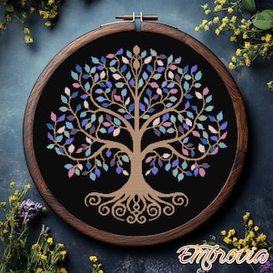 Peut inclure: Un motif de point de croix d'arbre de vie coloré avec un cerceau de broderie en bois brun. L'arbre a un tronc et des racines bruns et est rempli de feuilles bleues, vertes, roses et violettes.