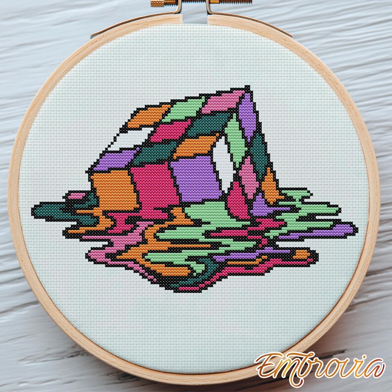 May include: A colorful cross-stitch design of a melting geometric shape, featuring shades of pink, orange, green, and purple. The artwork is set within a round wooden embroidery hoop, with the word "Embrovia" in the bottom right corner.