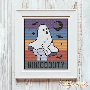 May include: Cross-stitch artwork in a white frame featuring a white ghost with the text "BOOOOOTY". The background has a sunset design with purple, blue, orange, and yellow stripes. Black bats and a crescent moon are also included.