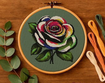 May include: A cross-stitch embroidery of a colorful rose in a wooden hoop. The rose features petals in shades of red, white, black, yellow, and blue, with green leaves. Embroidery floss in various colors is arranged nearby. The word "Embrovia" is in the bottom right corner.