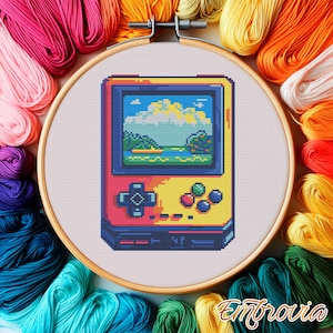 May include: A cross-stitch pattern of a retro handheld video game console with a pixelated landscape on the screen. The console is yellow, red and blue with a black and white control pad.