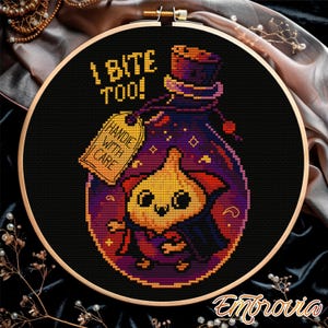 May include: Cross-stitch embroidery in a wooden hoop featuring a cartoon vampire cat in a potion bottle. The bottle is purple and has the text "I BITE TOO!" and "HANDLE WITH CARE" on a tag. The cat is orange and wearing a cape.