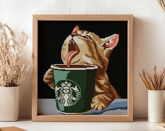 Puede incluir: Imagen de punto de cruz enmarcada que representa a un gato atigrado bebiendo café Starbucks. El gato, con la lengua fuera, bebe de una taza verde de Starbucks. La obra de arte está enmarcada en madera.