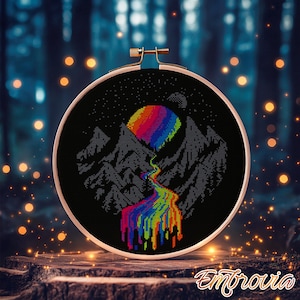 May include: Cross-stitch embroidery art in a wooden hoop. The design features a rainbow-colored sun or moon over gray mountains, with a rainbow river flowing down. The background is black with white stars.