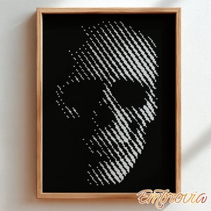 May include: A framed cross-stitch art piece featuring a stylized skull design. The skull is rendered in white stitches against a black background, creating a striking contrast. The frame is made of light-colored wood.