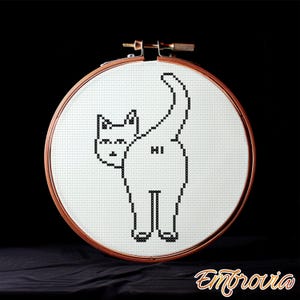 Könnte beinhalten: Ein Kreuzstich-Stickrahmen mit einem schwarz-weißen Katzendesign. Die Katze ist von hinten zu sehen, mit dem Wort "HI" auf ihrem Hinterteil gestickt. Der Rahmen ist rund mit einem Holzrahmen.
