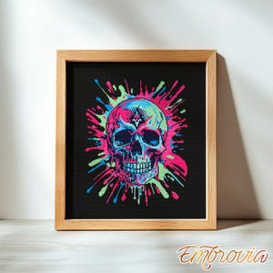 May include: A framed cross-stitch artwork depicting a vibrant skull design. The skull uses blue, pink, and green hues against a black backdrop. The frame is made of light wood. The artwork is signed "Embrovia".