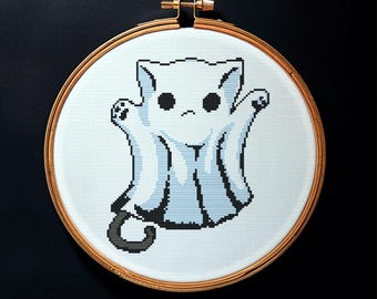 May include: A cross-stitch embroidery hoop featuring a white cat-shaped ghost with light blue accents. The cat has black eyes and a curved tail. The embroidery is set in a wooden hoop against a black background. The word "Embrovia" is in the bottom right corner.
