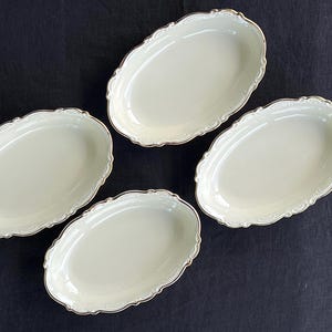 Op de afbeelding: Een set van vier ovale keramische schalen in een crèmewitte kleur. Elke schaal heeft een delicate, geschulpte rand met een dunne metallic gouden afwerking langs de rand, wat zorgt voor een verfijnde en consistente uitstraling van dit servies.