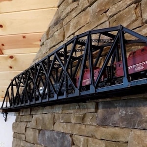 以下が含まれることがあります： 黒い金属製の鉄道模型の橋と赤い列車。 橋は石壁と木製の棚で支えられています。 列車には「ペンシルベニア」の文字が印刷されています。