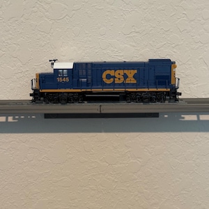 May include: A blue and yellow model train locomotive with the text "CSX" in gold. The number "1545" is visible on the side. The train is on a gray track.