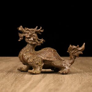 以下が含まれることがあります： 龍とカメのハイブリッドである、神話上の生き物のブロンズ色の像。 彫刻には、鱗、ドラゴンの頭、背中のカメの甲羅など、複雑なディテールが施されています。 像は木製の表面にあります。