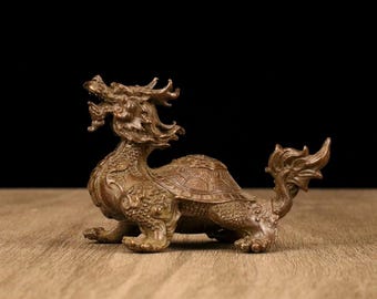 May include: A bronze-colored statue of a mythical creature, a hybrid of a dragon and a turtle. The sculpture has intricate details, including scales, a dragon's head, and a turtle shell on its back. The statue is on a wooden surface.