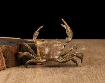 May include: A bronze crab sculpture with raised claws and detailed legs. The crab is positioned on a wooden surface, showcasing its intricate design and texture. The sculpture has a dark brown patina.