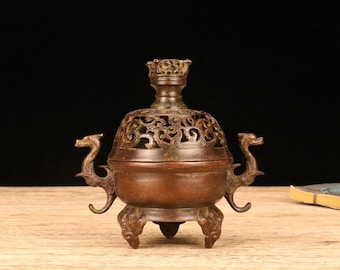 May include: A bronze incense burner with a decorative, openwork lid and dragon-shaped handles. The burner has three ornate feet and a detailed, textured surface. The overall design is antique and traditional.