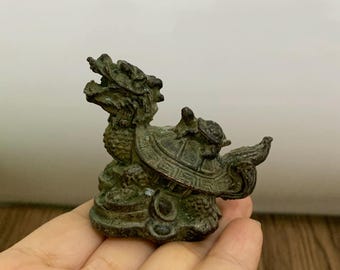 May include: A small, bronze-colored figurine depicting a mythical creature with a dragon's head and a turtle's body. The detailed sculpture features intricate patterns and textures, showcasing a blend of animal forms. The figurine is approximately 3 inches long.