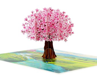 May include: A 3D pop-up greeting card featuring a cherry blossom tree with pink flowers and a brown trunk. The card is open, revealing a colorful landscape scene. The card is on a white background.